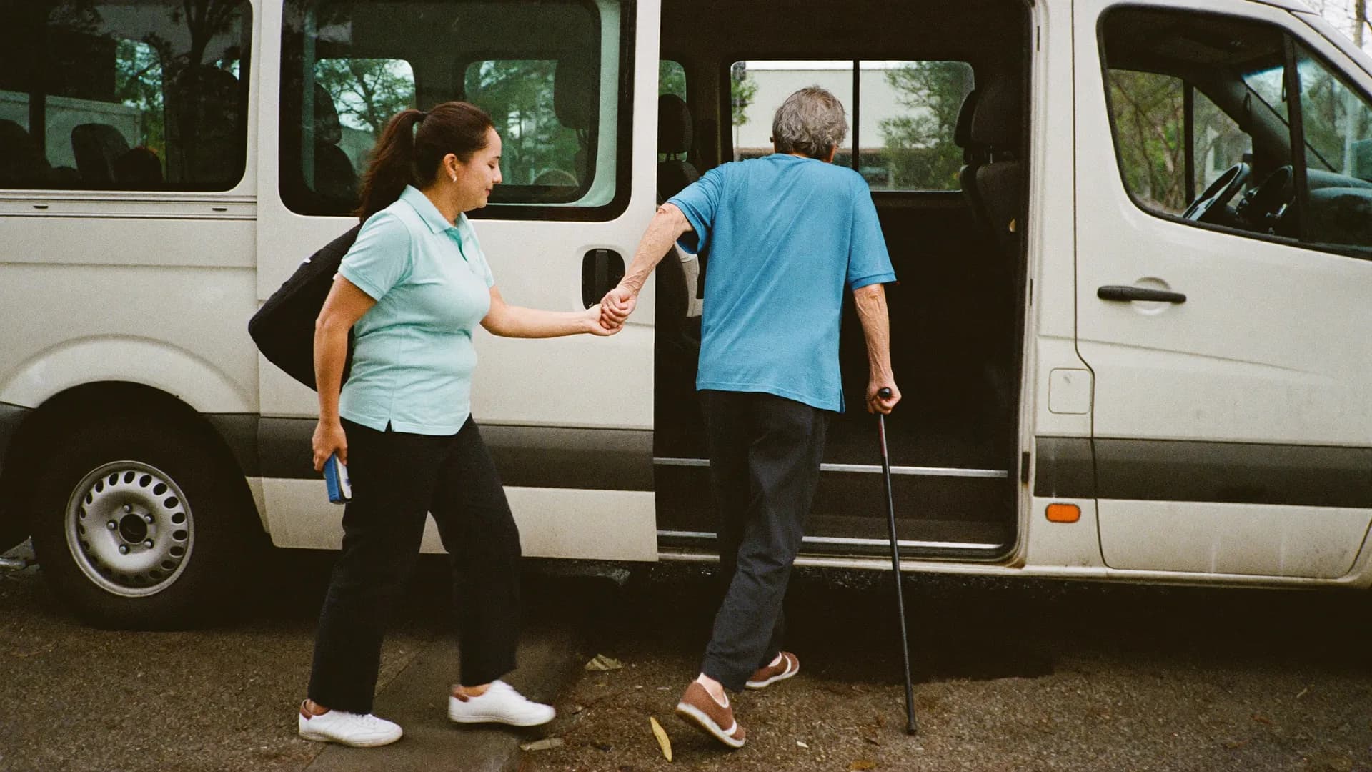 A driver holds a rider’s hand as he steps up into the van with his cane